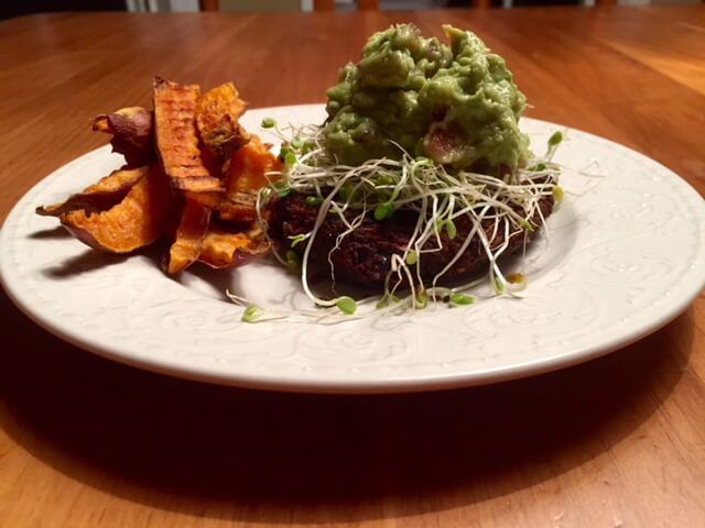 Black bean burger topped with guacamole on a plate with sweet potatoes